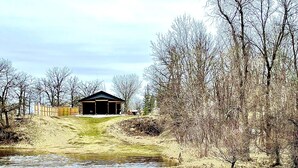 Une vue sur la rivière, avec un bâtiment perché sur une colline verdoyante, entouré d’arbres sans feuilles.