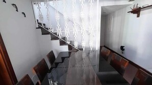 A modern dining area with a long wooden table and matching benches. A staircase with a decorative railing leads to an upper level. - Cobertura Duplex - Santos (Santos)