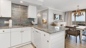 A modern kitchen with white cabinetry, a marble countertop, and a brick backsplash.