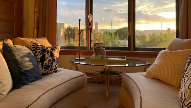 A cozy living room with a large window, a round glass table, and two sofas with patterned cushions. - •1898UrbanVictorian Loft view near Convention Ctr. (Portland)