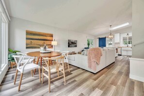 A modern living room with a dining area, a sofa, and a kitchen in the background. - Waterfront Retreat | Millers Bay Canal Getaway (Milford)