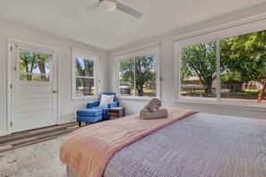 A bedroom with a bed, a chair, a desk, and large windows. - Waterfront Retreat | Millers Bay Canal Getaway (Milford)