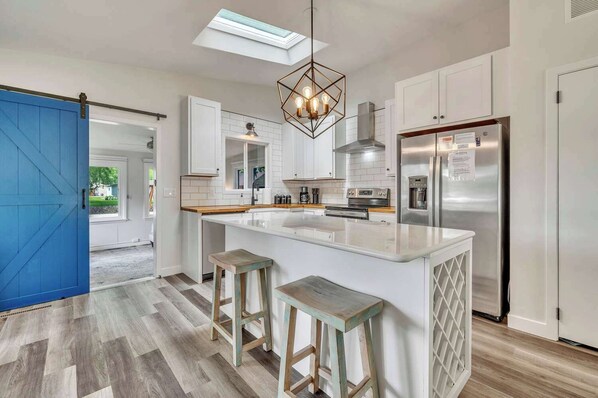 A modern kitchen with a central island, bar stools, a stainless steel refrigerator, and a skylight.