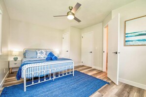 A bedroom with a bed, a ceiling fan, a nightstand, a blue rug, and a door. - Boji Waterfront Retreat - Millers Bay Canals (Milford)