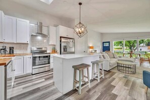 A modern kitchen with white cabinetry, stainless steel appliances, and a central island with stools. - Waterfront Retreat | Millers Bay Canal Getaway (Milford)