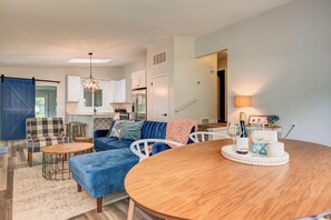 A modern living room with a blue sofa, a wooden coffee table, and a dining table with a tray.