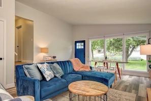 A living room with a blue sofa, a round wooden coffee table, and a view of the outdoors through large windows.