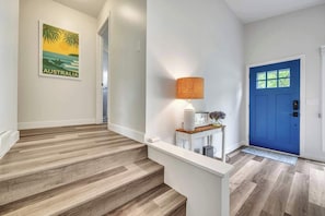 A hallway with wooden flooring, a blue door, a wall-mounted lamp, and a framed picture. - Waterfront Retreat | Millers Bay Canal Getaway (Milford)