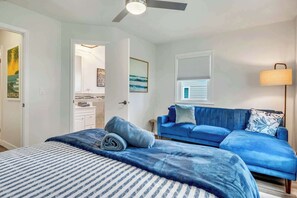 A bedroom with a bed, a blue sofa, a window with blinds, and a ceiling fan.