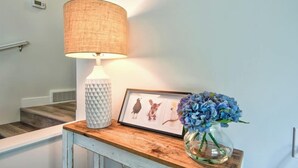Una lámpara, una obra de arte enmarcada y un jarrón con flores sobre una mesa de madera.