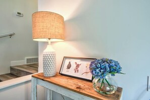 Una lámpara, una obra de arte enmarcada y un jarrón con flores sobre una mesa de madera.