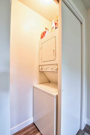 A compact laundry room with a washing machine and dryer, a small shelf with items, and a door leading to another room. - Boji Waterfront Retreat - Millers Bay Canals (Milford)