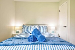 A bed with striped bedding, two pillows, a rolled towel, and two bedside lamps. - Boji Waterfront Retreat - Millers Bay Canals (Milford)