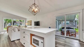 Una cocina moderna con una isla central, electrodomésticos integrados y un comedor con mobiliario de exterior.