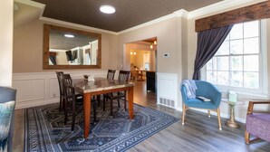A dining area with a wooden table and chairs, a patterned rug, and a large mirror on the wall. - Family House (Omaha)