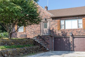 A two-story brick house with a stone retaining wall, a wooden bench, and a garage. - Family House (Omaha)