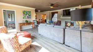 A spacious living room with a grey sectional sofa, patterned armchairs, a wooden coffee table, and a ceiling fan. - Family House (Omaha)