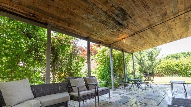 An outdoor patio with a covered seating area, stone flooring, and surrounding greenery. - Family House (Omaha)
