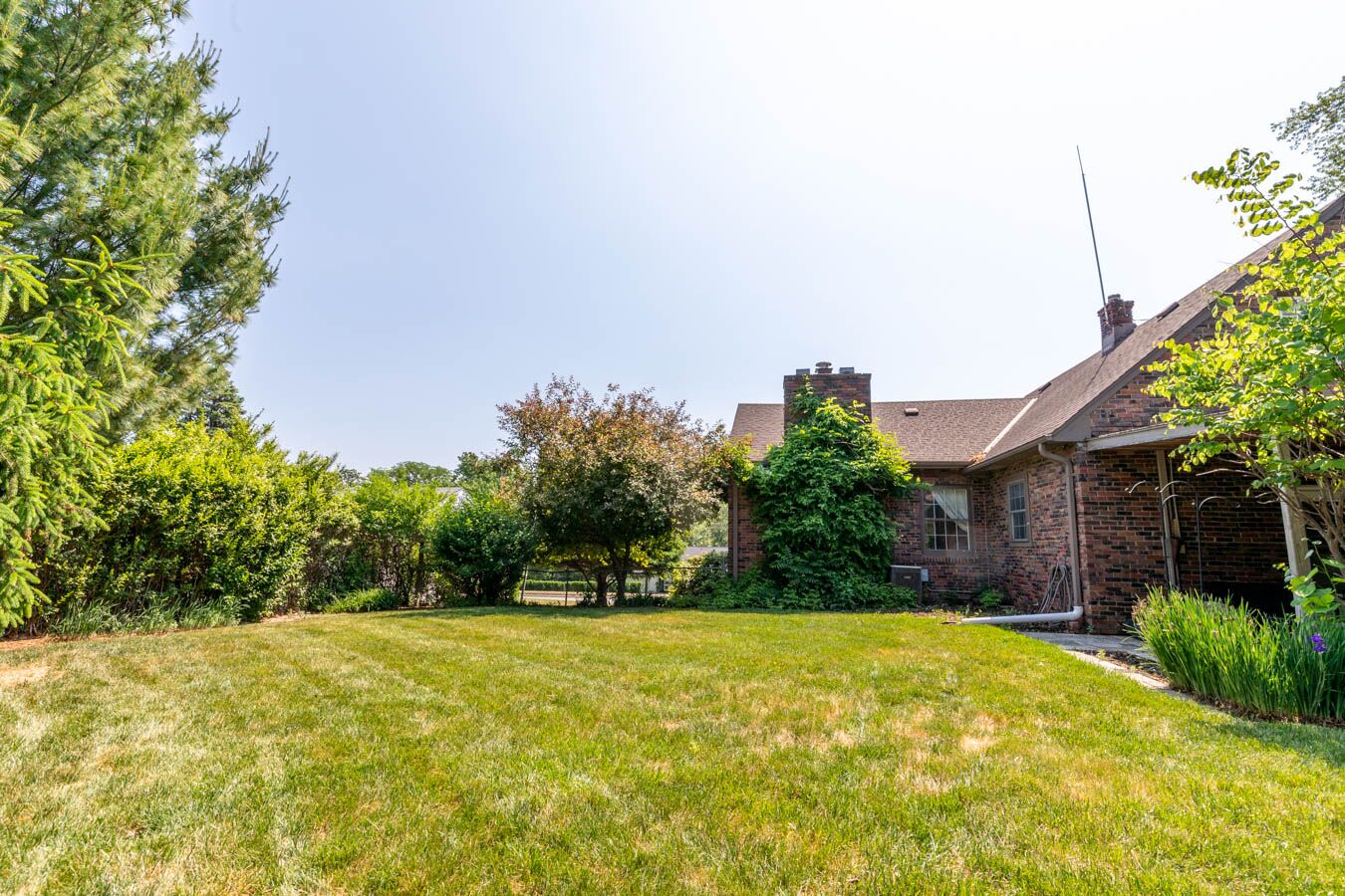 A brick house with a well-maintained lawn and various trees.