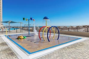 Un espace de jeux aquatiques avec des anneaux colorés et une fontaine, entouré d’une piscine et offrant une vue sur la plage.