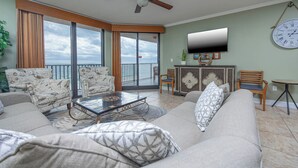 A spacious living room with a large sofa, a coffee table, and a television mounted on the wall. There is a balcony with a view of the ocean. - Stunning 3 Bedroom Condo Phoenix X 710 (Agadir)