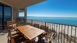 A balcony with a wooden table and chairs, overlooking a beach with a clear blue sky. - Stunning 3 Bedroom Condo Phoenix X 710 (Agadir)