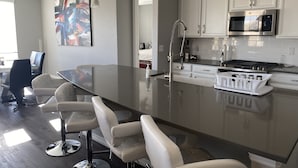 A modern kitchen with a large island, white cabinets, stainless steel appliances, and bar stools.
