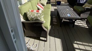 A covered outdoor area with a green sofa, wicker chairs, a table, and a barbecue grill.