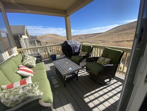 A covered outdoor deck with a green sofa, wicker chairs, a table, and a barbecue grill.