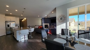 A modern kitchen with a central island, dining area with chairs, and a fireplace.