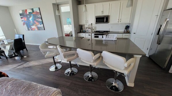 A modern kitchen with a central island, white cabinetry, stainless steel appliances, and a dining area with bar stools.