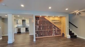 A spacious living area with a wooden wine rack, a staircase, and a kitchen in the background.