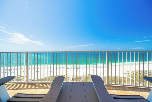 Un balcon avec deux fauteuils de jardin donnant sur une plage aux eaux turquoise et au sable blanc.
