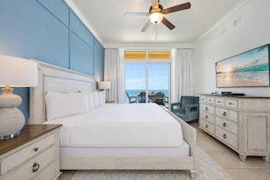 Habitación de hotel con una cama grande, un ventilador de techo, televisión, cómoda y vista al océano.