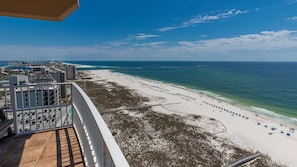 A beach view from a balcony with a clear sky, a sandy beach, and a calm sea.