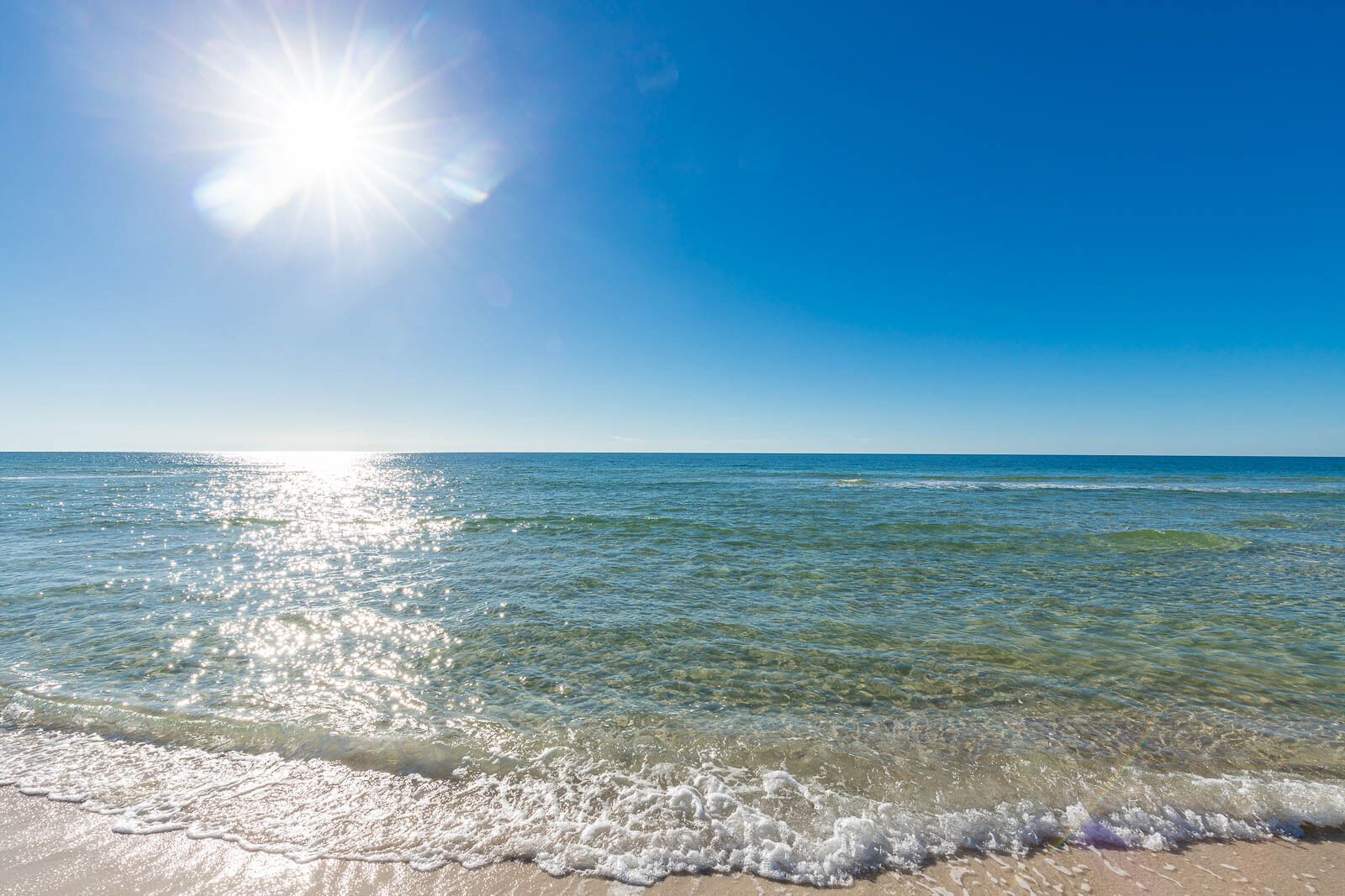 Una playa con agua cristalina, olas y un sol brillante.