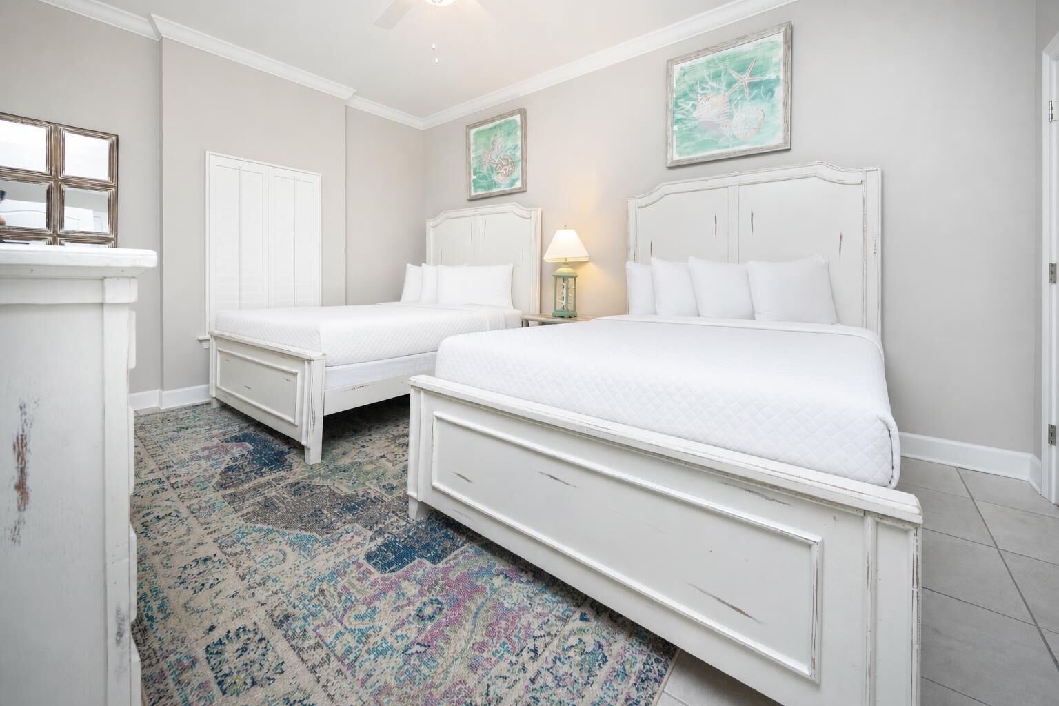 Une chambre à coucher avec deux lits blancs, un tapis à motifs et une petite table avec une lampe.