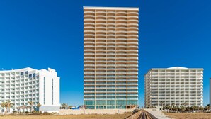 A tall hotel with multiple balconies, a beach boardwalk, and palm trees.