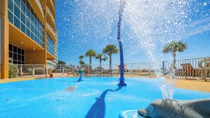 Una fuente de agua con una escultura de delfín, rodeada de palmeras y un edificio con amplias ventanas.