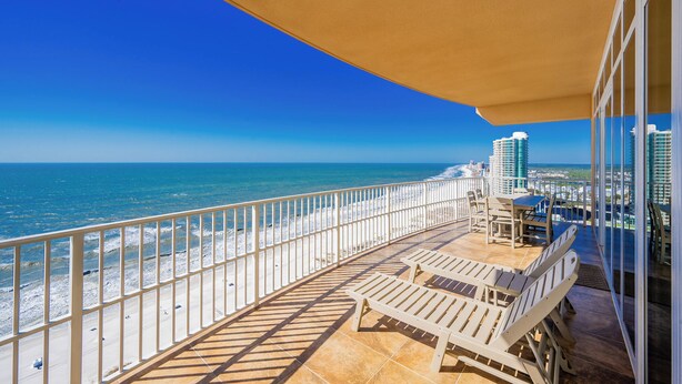 Un balcón con vistas a la playa y al océano, amueblado con sillones y una mesa.