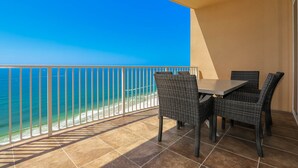 A balcony with a view of the ocean, a table, and wicker chairs.