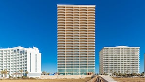 A tall hotel with multiple balconies, a beach boardwalk, and palm trees.