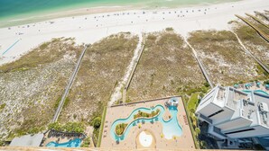 An aerial view of a beach resort with a swimming pool, beach umbrellas, and a boardwalk.