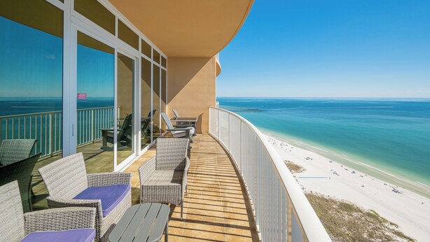 A balcony with wicker furniture, a view of the ocean, and a sandy beach.