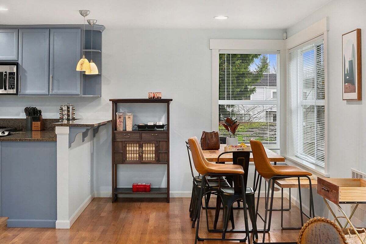 Ett modernt kök med gråa skåp, en köksö i trä och en matplats med bord och stolar.