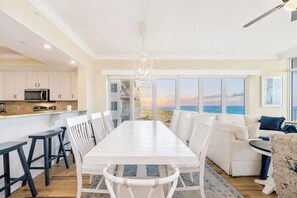 A modern kitchen with white cabinets, a dining area with a white table and chairs, and a view of the ocean through large windows. - 🌊☀Phoenix Orange Beach II 405 - Beautiful Gulf Front Condo at BRAND NEW PhOB2☀🌊 (Orange Beach)