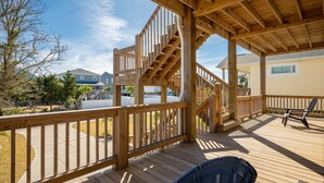 A wooden deck with a staircase leading to a covered area, surrounded by a fence and trees. - Beach 45: Large, Modern Home Situated on the Davis Canal, Around 500 Feet to Bea (Oak Island)