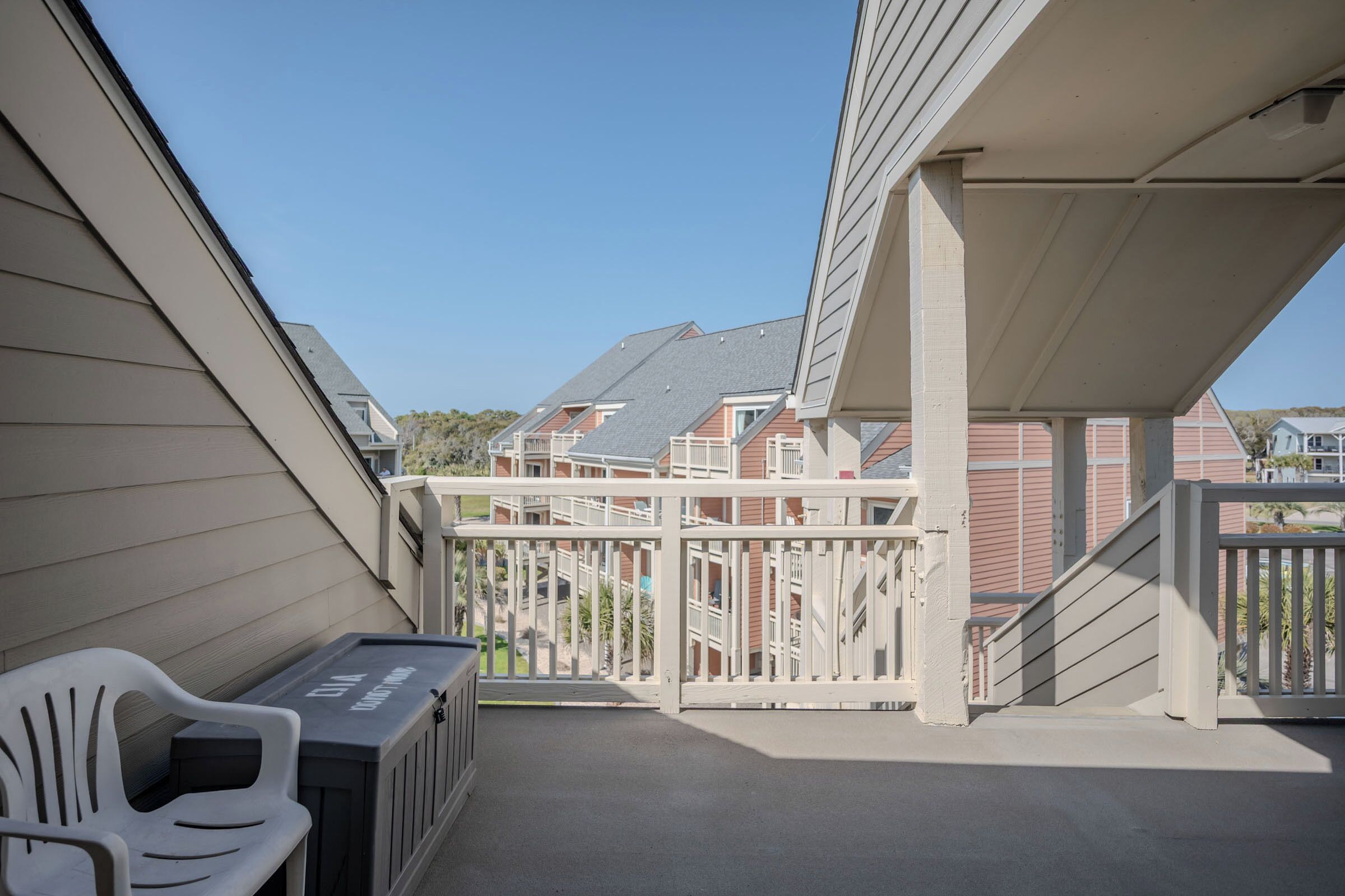 A balcony with a white railing, a trash bin, and a white plastic chair.