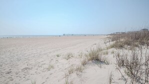 A sandy beach with dunes and a pier extending into the water.