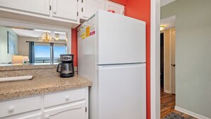 A kitchen with white cabinets, a white refrigerator, a coffee maker, and a window with curtains.
